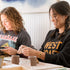 Two women sitting at a table with clay pots, engaged in a craft activity.